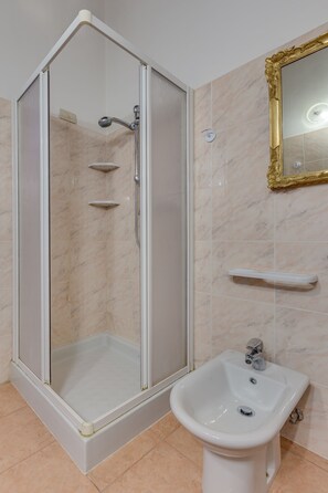 A bathroom with a shower enclosure, a pedestal sink, and a mirror with a gold frame. - Venezianamente - Dimora Furlani Canal view (Venice)