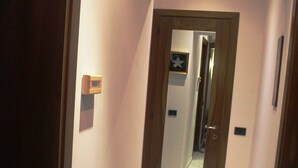 A narrow hallway with a wooden door, a small light fixture, and a mirror on the wall. - Venezianamente-Casa della Crea Canal (Venice)