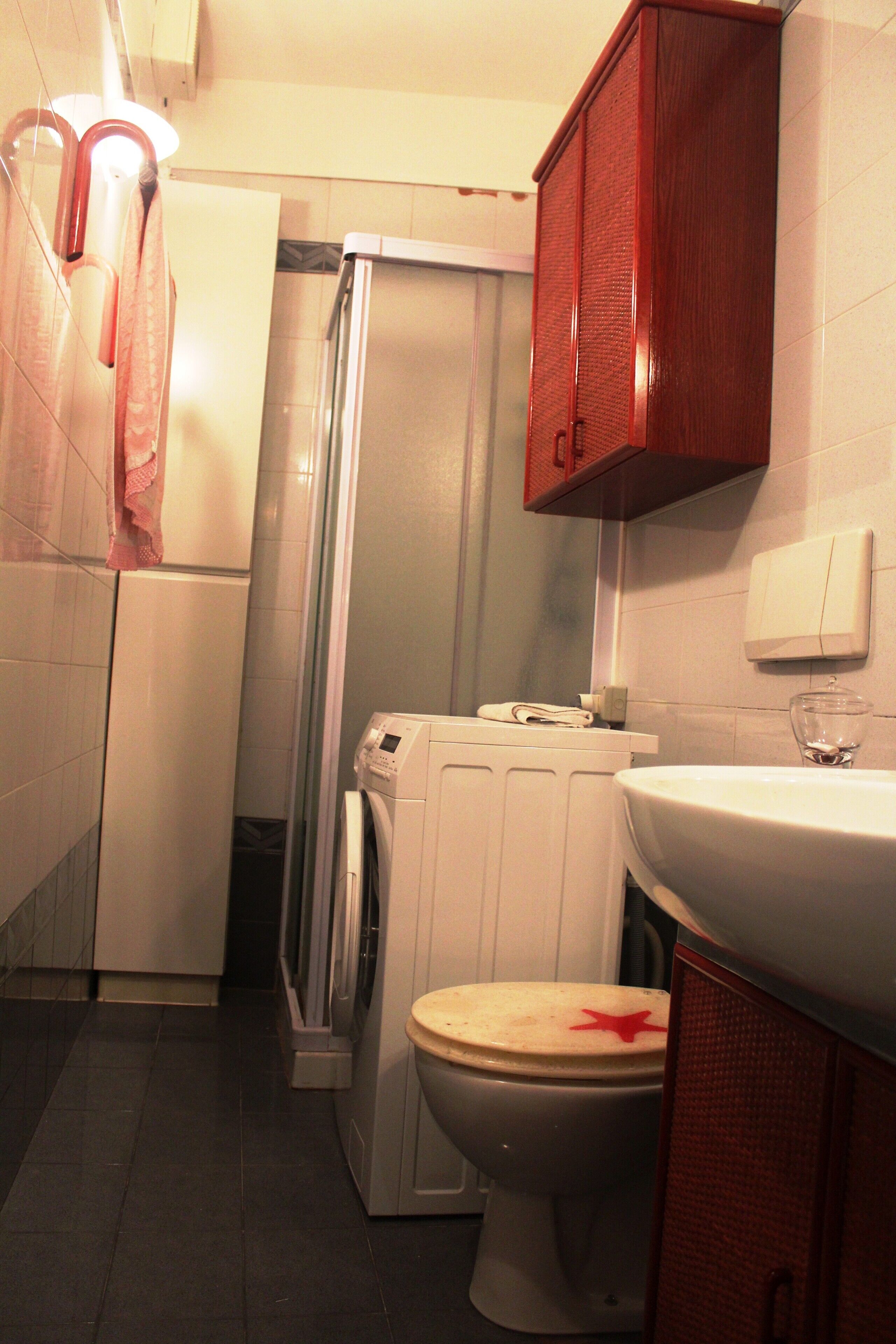 A compact bathroom with a toilet, a washing machine, and a cabinet.