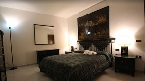 A bedroom with a large bed, a headboard with artwork, two bedside tables with lamps, a floor lamp, and a mirror on the wall. - Venezianamente-Casa della Crea Canal (Venice)