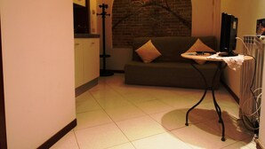 A narrow hallway with a tiled floor, a sofa with cushions, a small table with a lamp, and a brick wall with a light fixture. - Venezianamente - Residenza Formosa (Venice)