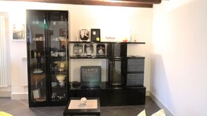 Ein Wohnzimmer mit einer Couch, einem Fernseher und einer Vitrine mit diversen Gegenständen.