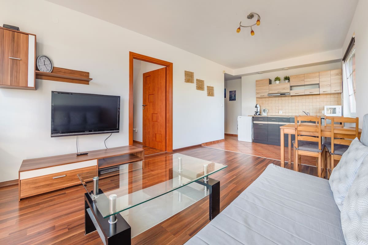 Ein modernes Wohnzimmer mit Fernseher, Holzmöbeln, einem Glastisch und einer Couch.