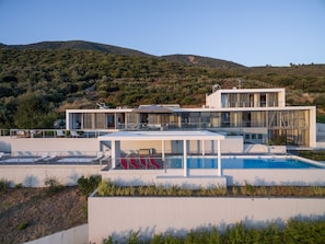 Una casa moderna de dos pisos con piscina, amplias ventanas y vistas a un paisaje montañoso.