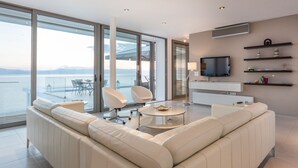A modern living room with a large sofa, a coffee table, and a TV. There is a balcony with a view of the sea. - 600m² homm Luxury Villa Sea Side Evia 16ppl (Istiaia-Aidipsos)
