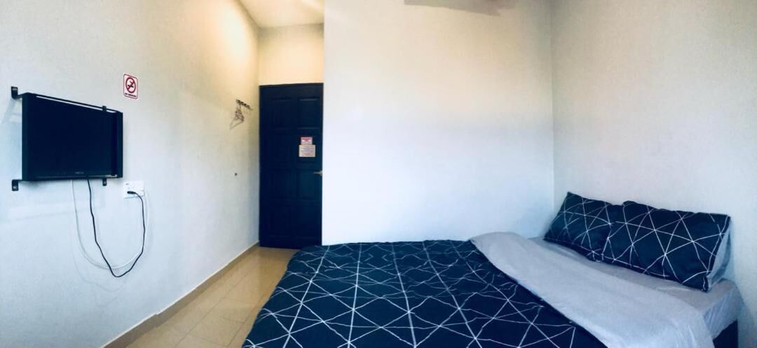 Una stanza piccola e modesta con un letto, una TV a parete e una porta.