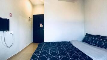 A small, simple room with a bed, a TV mounted on the wall, and a door.
