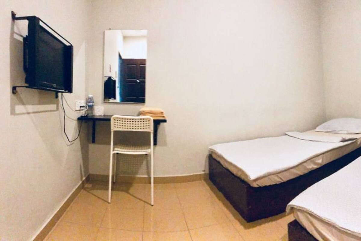 A small, simple room with two beds, a desk, a chair, and a TV.