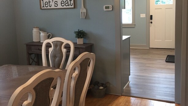 Un'area pranzo con un tavolo e sedie in legno, un cartello appeso al muro con la scritta “let's eat”, una piccola pianta e un termostato.