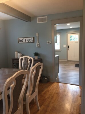 A dining area with a wooden table and chairs, a wall-mounted sign saying "let's eat", a small plant, and a thermostat. - Cozy home, short walk to Crystal Lake (Beulah)