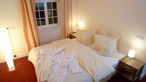 Un lit bien fait, avec du linge de lit blanc et des oreillers, une table de chevet avec une lampe et une fenêtre avec des rideaux.