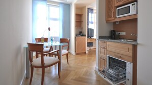 Une cuisine moderne équipée d’un four à micro-ondes encastré, d’un lave-vaisselle et d’une machine à café. On y trouve également un coin repas avec une table en verre et des chaises en bois.
