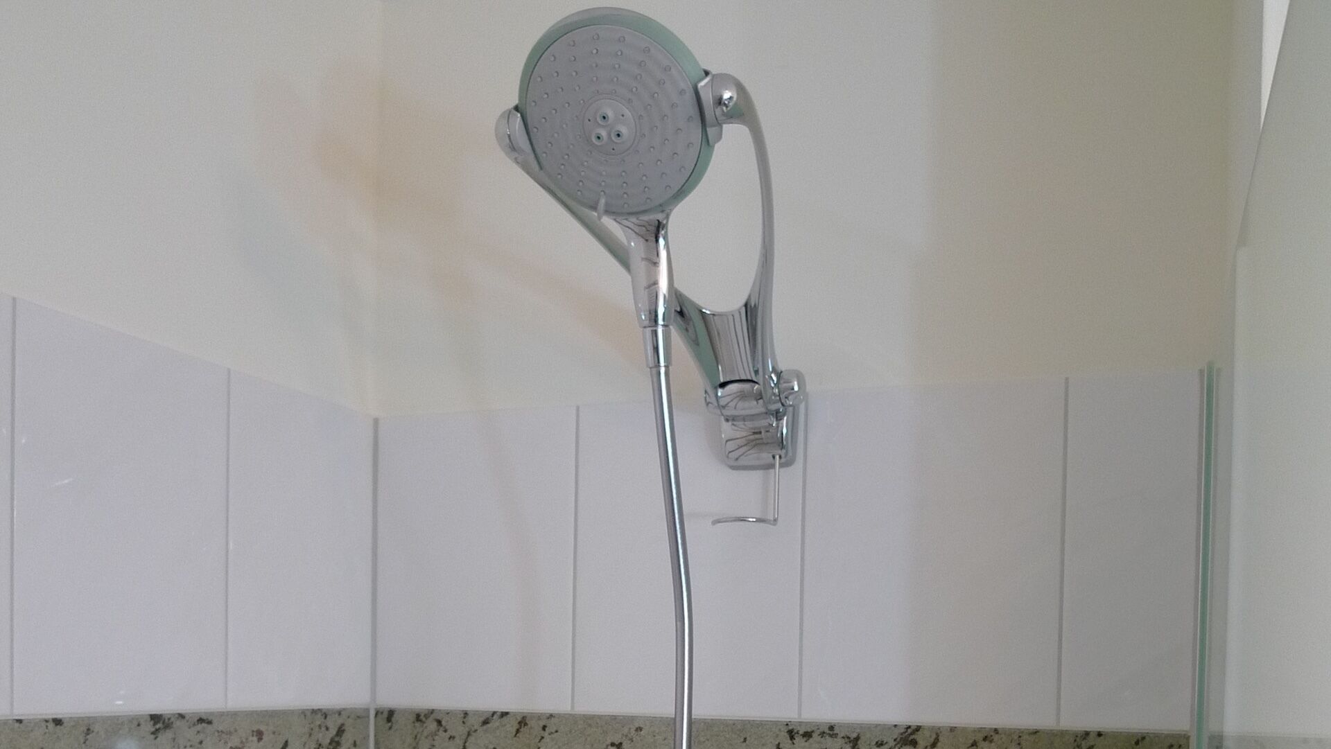 A showerhead with a flexible hose, mounted on a wall with white tiles.
