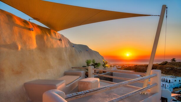 Una terraza iluminada por el sol con vistas a la puesta de sol, paredes blancas y mobiliario exterior.