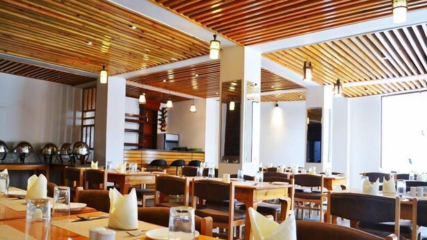 Un restaurant avec des panneaux de bois au plafond, plusieurs tables où l’on peut manger, avec des serviettes blanches, et un bar situé au fond de la salle.