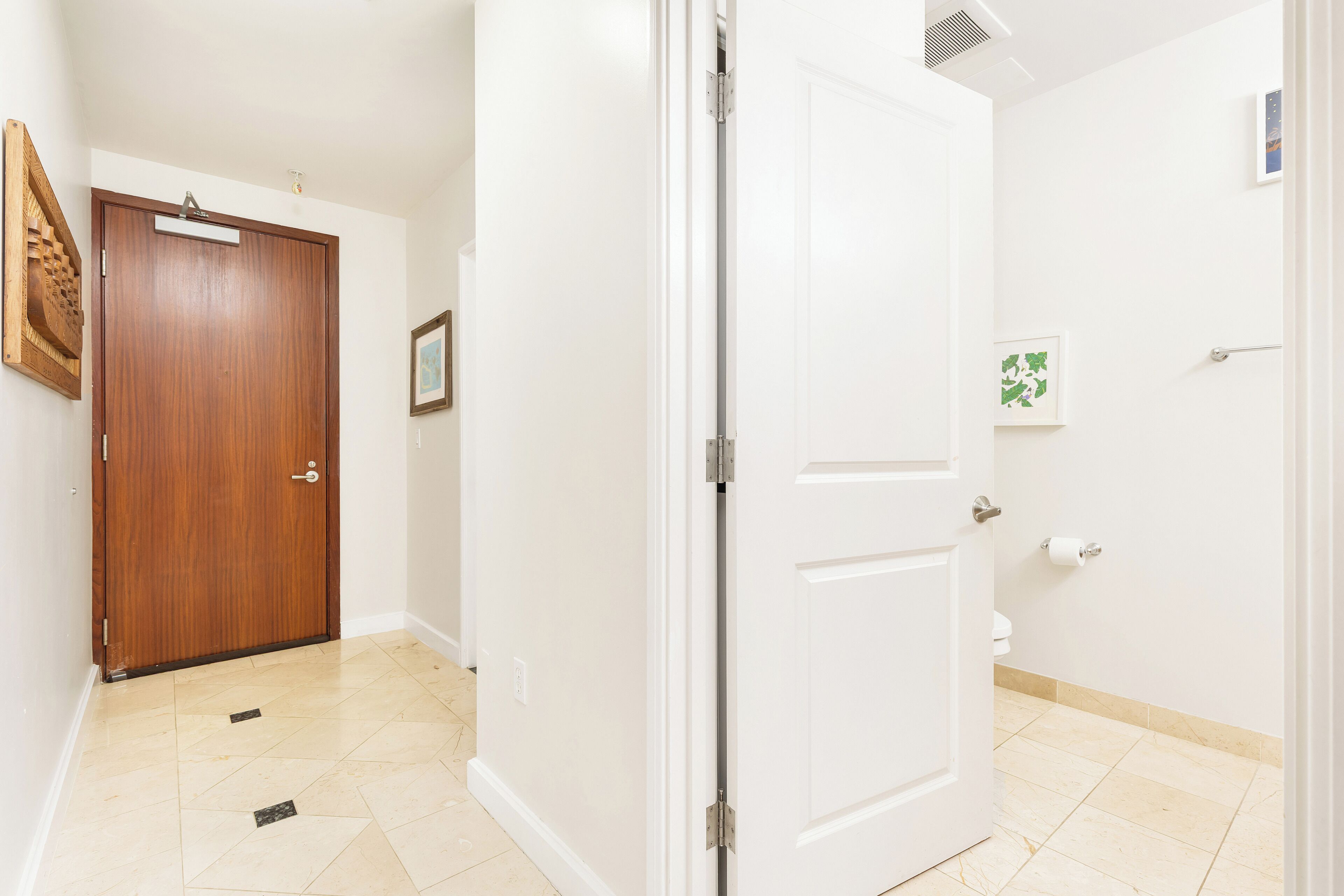 Un couloir avec une porte en bois, une porte blanche et des toilettes équipées d’un porte-rouleau de papier toilette.