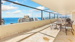 A balcony with a view of the ocean and cityscape, furnished with a table and chairs.