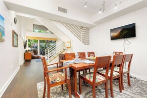Un comedor con mesa y sillas de madera, una escalera y un televisor montado.