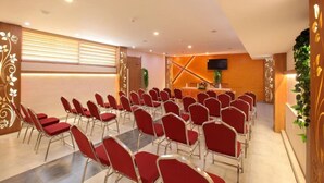 A conference room with rows of red chairs, a podium, and a television screen. - Pushpak Grande (Kondotti)