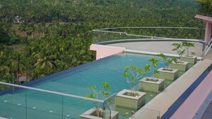 A rooftop infinity pool with clear blue water, surrounded by palm trees and a lush green landscape. - Pushpak Grande (Kondotti)
