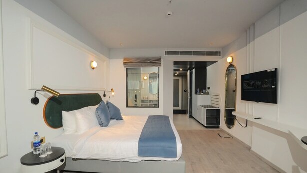 A modern hotel room with a large bed, bedside tables, a flat-screen TV, and a walk-in closet. - Pushpak Grande (Kondotti)
