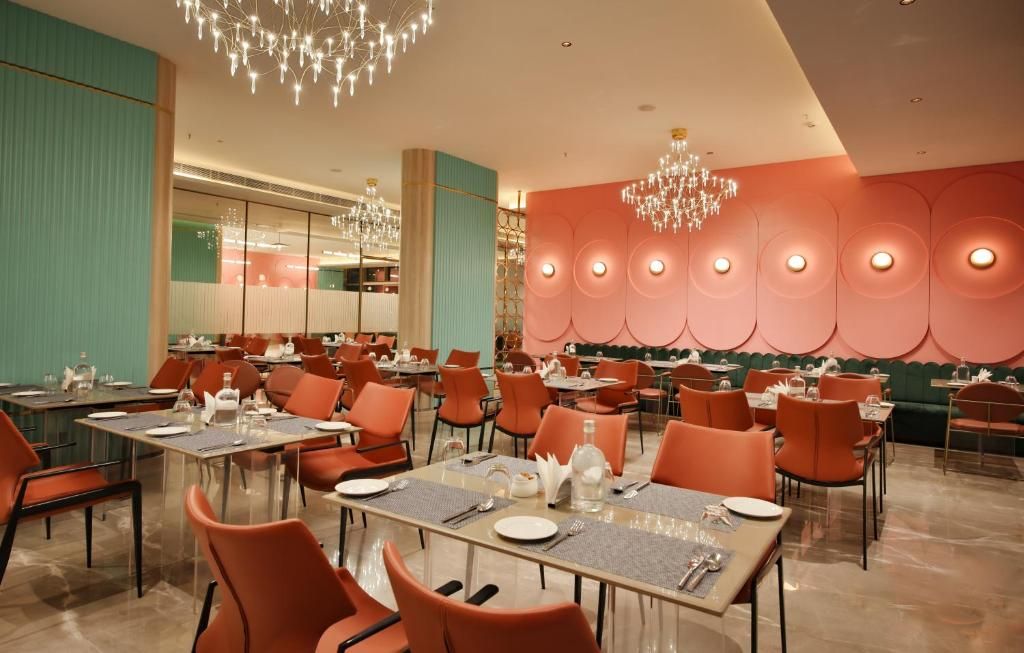 A dining area with tables and chairs, chandeliers, and a wall with circular light fixtures.