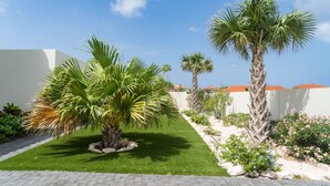 Un giardino curato con palme, un vialetto lastricato e un edificio bianco con tetto rosso.
