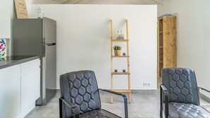 Una cucina moderna con un frigorifero in acciaio inox, due poltrone in pelle nera, una mensola in legno con spazio contenitivo e un armadietto in legno.