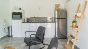 Una cucina moderna con mobili bianchi, un frigorifero in acciaio inossidabile, una sedia nera e una mensola in legno con una pianta.