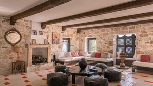 Uma sala de estar rústica com paredes de pedra, lareira, pufes de couro e um conjunto de sofá.