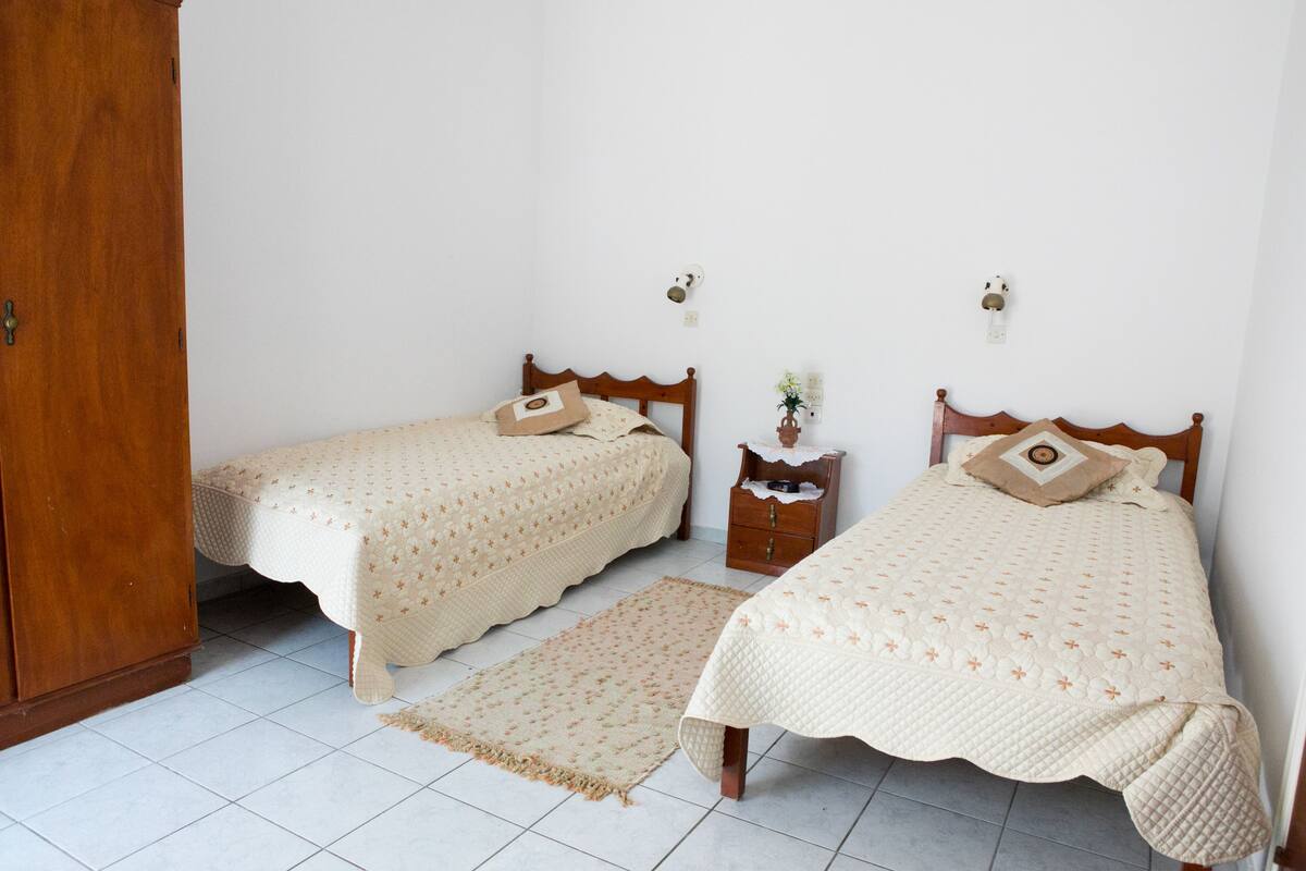 Two single beds with matching headboards and footboards, a wooden nightstand with a lamp, and a small table with a vase of flowers.