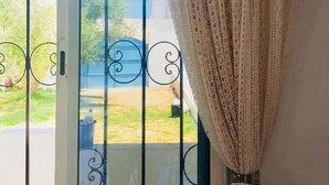 A room with a large window featuring a metal gate, a curtain, and a view of a green outdoor area. - Dar Aesha (Aghir)