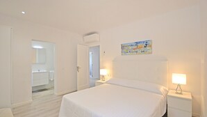 A bedroom with a bed, two bedside tables with lamps, a painting on the wall, and a bathroom visible through an open door. - Pinocha - House with private pool 300 meters from the beach in Mallorca (Can Picafort)