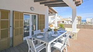 An outdoor patio with a table set for dining, white chairs, and a view of the sea. - Pinocha - House with private pool 300 meters from the beach in Mallorca (Can Picafort)