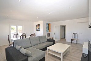 Una sala de estar moderna con un sofá seccional gris, una mesa de centro blanca y un comedor con sillas de madera.