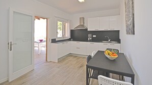 A modern kitchen with white cabinetry, a black countertop, and a dining area with a table and chairs. - Pinocha - House with private pool 300 meters from the beach in Mallorca (Can Picafort)