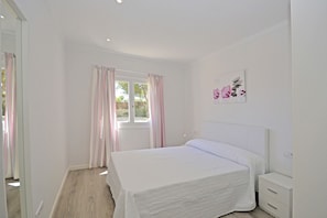 Un dormitorio con cama, mesita de noche, ventana con cortinas y una obra de arte colgada en la pared.