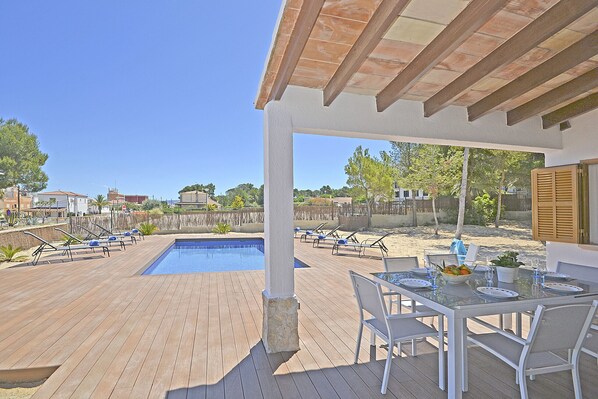 Un área junto a la piscina con mesa y sillas, piscina y sillones de descanso.