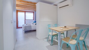 A modern room with a wooden ceiling, a bed with a view, a table with chairs, and an air conditioning unit.