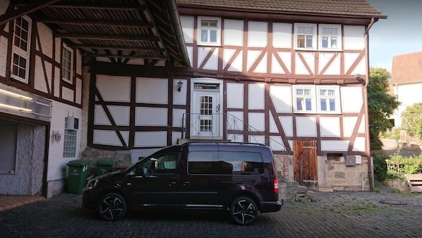 A black van parked in front of a traditional half-timbered house with a garage. - Baunaeck (Baunatal)