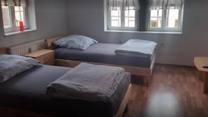 A room with two beds, a wooden floor, a window with curtains, a small desk with a chair, and a TV on a stand. - Baunaeck (Baunatal)
