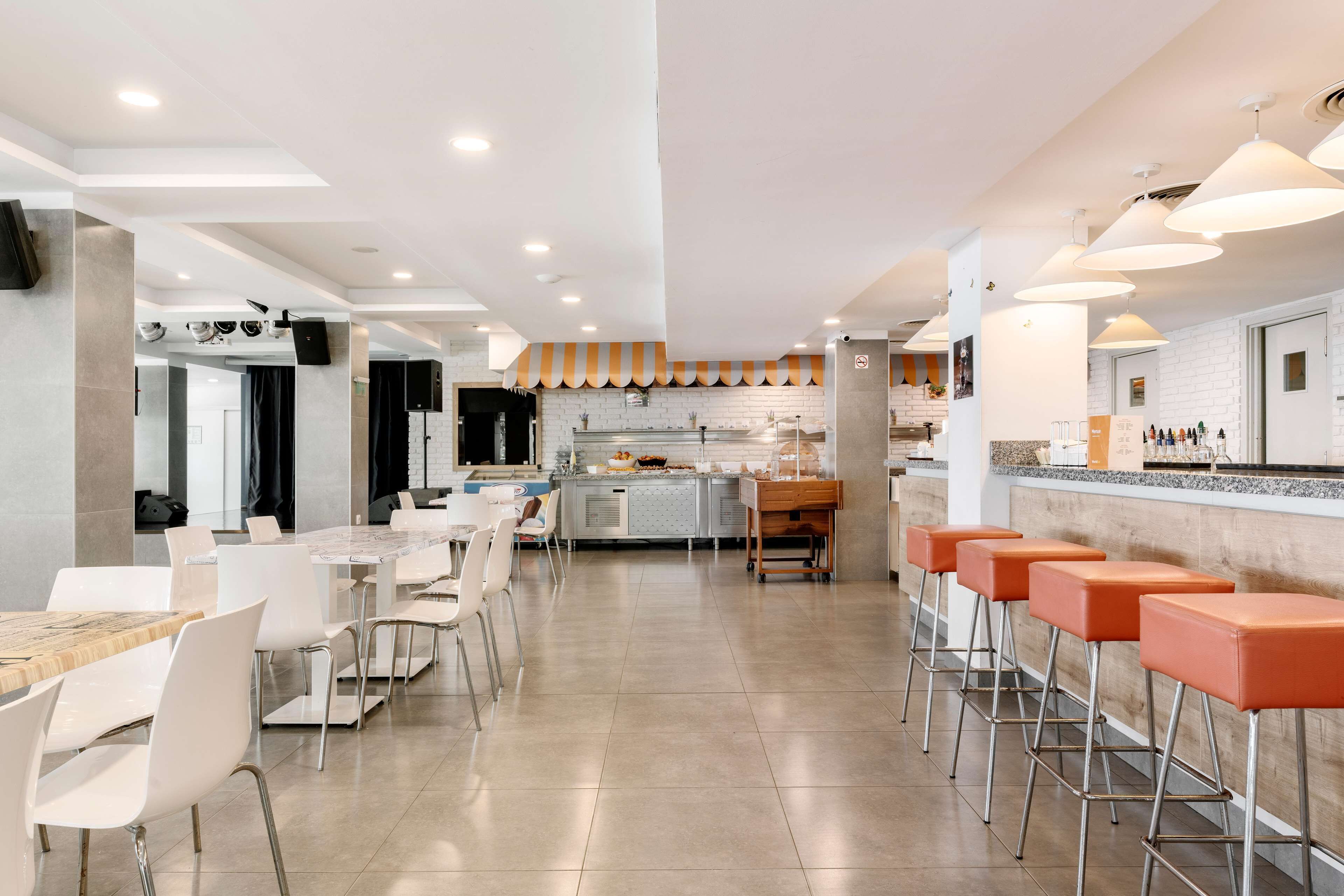 A modern kitchen with a central island, bar stools, and a long dining table with chairs.