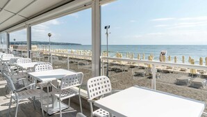 An outdoor seating area with white tables and chairs, overlooking a beach with umbrellas and lounge chairs. - AluaSun Helios Beach – All Inclusive (Obzor)