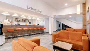 Un área de recepción con asientos naranja, una barra con mostrador blanco y una escalera que conduce a un nivel superior.