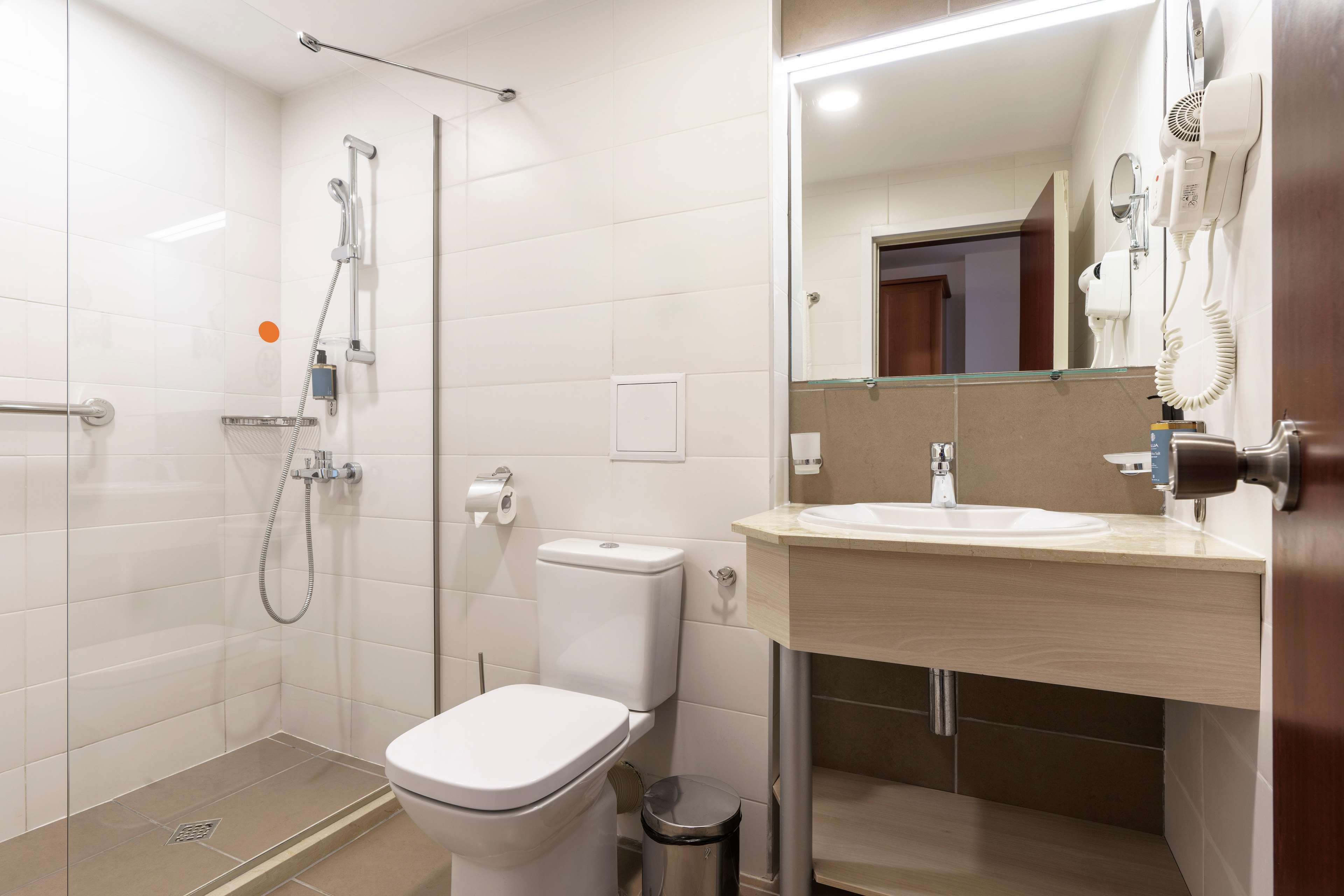 A modern bathroom with a shower, toilet, sink, and a mirror.