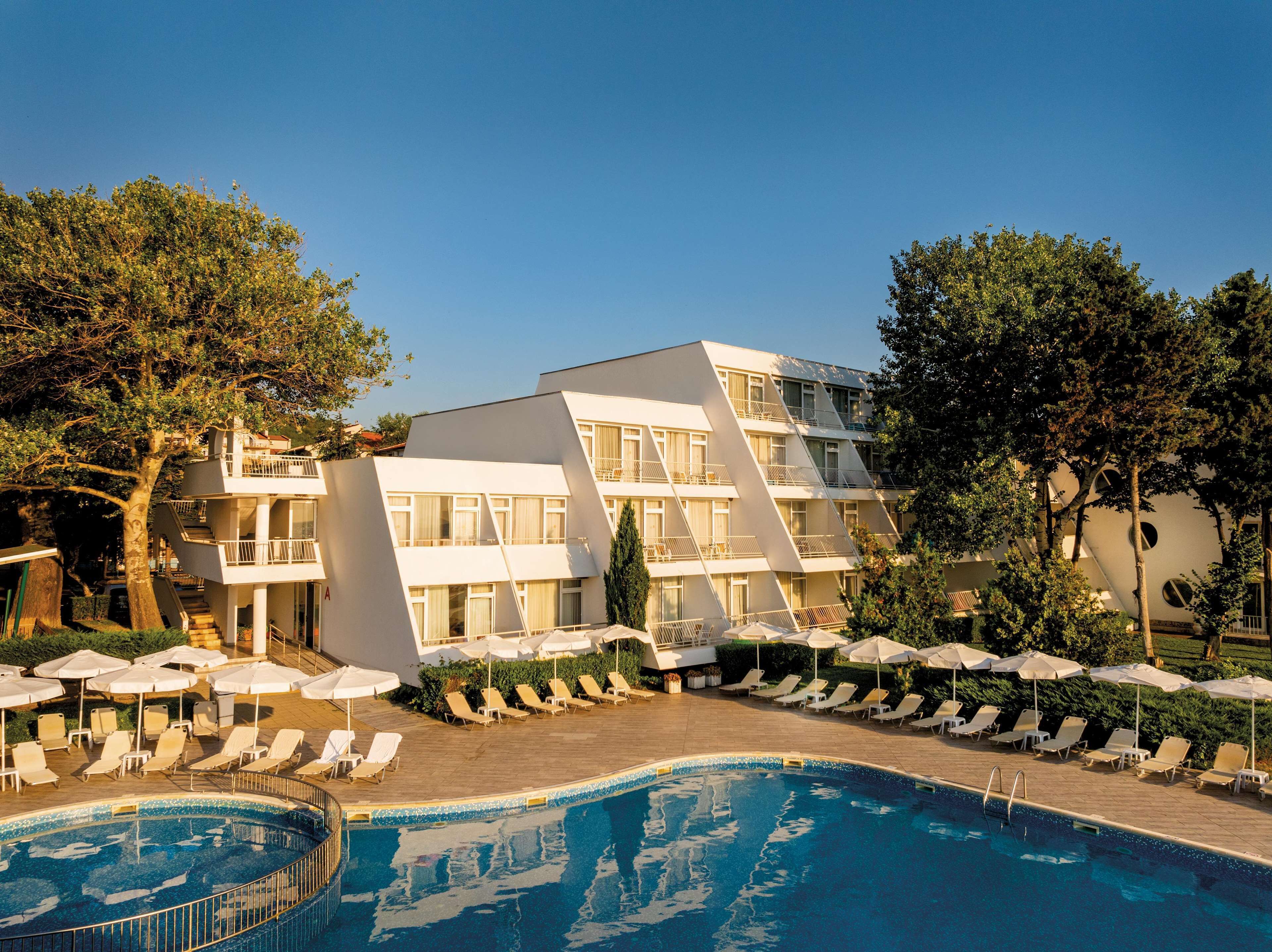 A modern hotel with a pool, multiple balconies, and sun loungers.