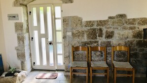 A stone-walled room with a white door, two wooden chairs with checkered cushions, and a stone bench. - A holiday in unspoiled nature (Modica)