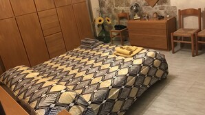 A bedroom with a patterned bedspread, wooden wardrobe, a dresser, a chair, and a mirror on the wall. - A holiday in unspoiled nature (Modica)
