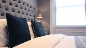 A neatly made bed with a tufted headboard, two pillows, and a bedside lamp. - The Hayden Pub & Rooms (London)