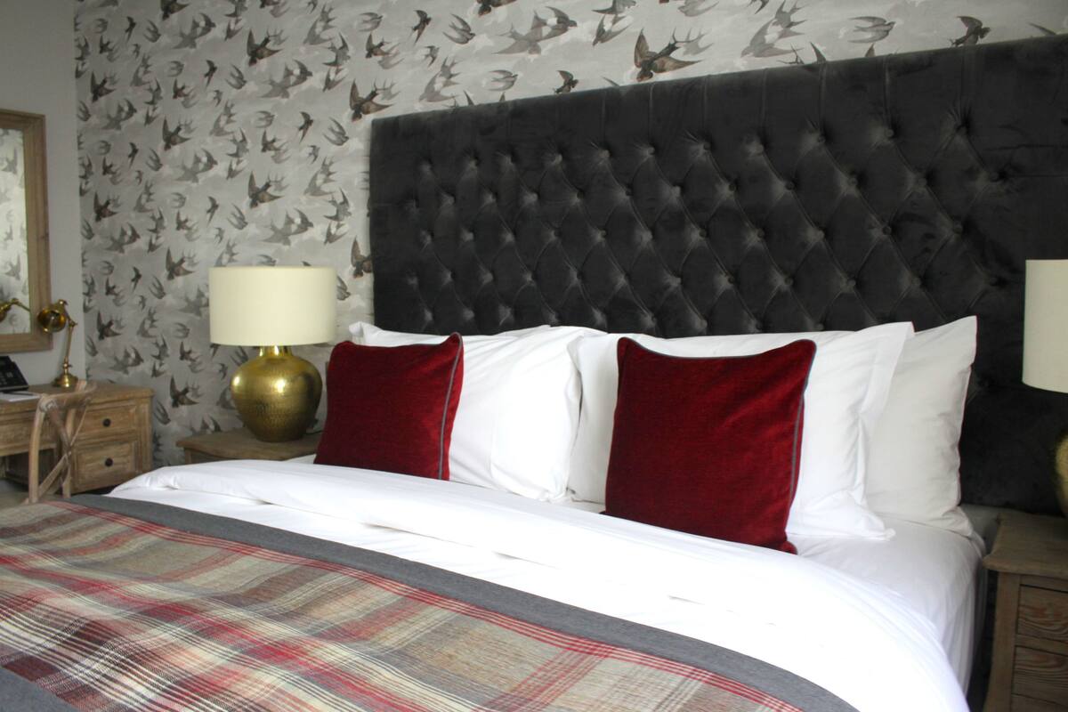 A hotel room with a tufted headboard, a plaid bedspread, and red and white pillows.